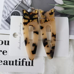 A pair of tortoiseshell cat-ear hair clips with gold eyes, whiskers, and ears, attached to a white card