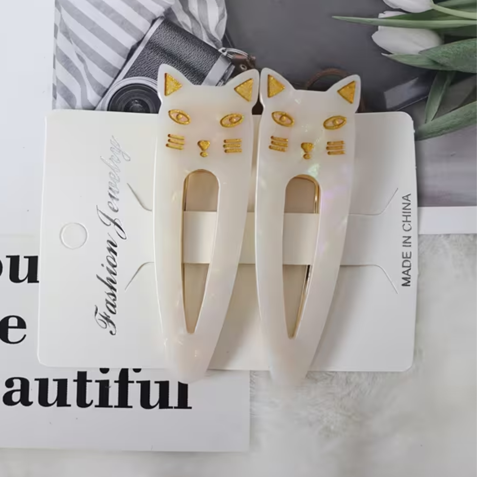 A pair of opal-white cat-shaped hair clips with gold accents, displayed on a white card