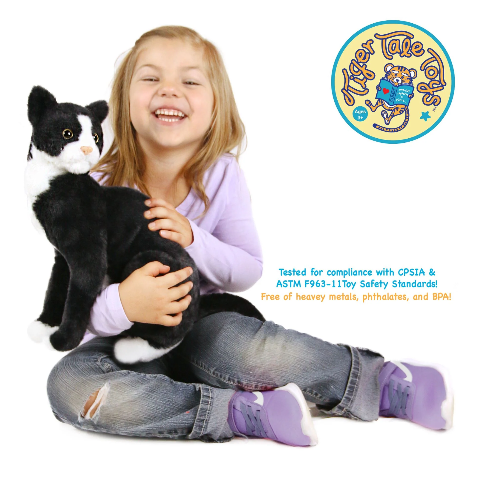 A smiling young girl playing with a plush black and white cat toy with safety text.