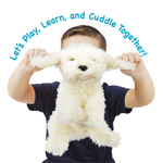 A child wearing a navy blue shirt holds up a fluffy white plush dog toy with floppy ears. Blue text curved over the top reads, 'Let's Play, Learn, and Cuddle Together!' on a plain white background.