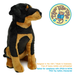 A plush toy dog in a black and tan Rottweiler-style coat, shown sitting on a white background with a Tiger Tale Toys logo in the upper right and product  safety text at the bottom.