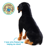 A black and tan plush dog toy shown from the back on a white background, with a circular TigerHart Toys logo in the top-left and text at the bottom stating 'I have wire-framed legs helping me stand!'.