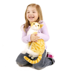 A young girl with blonde hair smiling and hugging a plush orange and white tabby cat toy, kneeling on a white background.