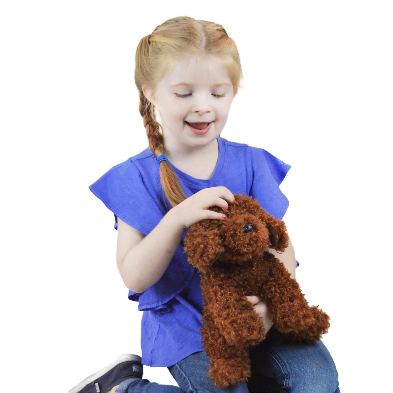 A young girl with blonde pigtails wearing a blue ruffled shirt and jeans, smiling while holding a brown curly-haired plush dog toy against a solid white background.