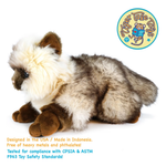 A plush toy cat with fluffy cream, gray, and brown fur, lying down on a white background. A circular 'Tiger Tale Toys' logo is in the top right, and text at the bottom mentions USA and Indonesia manufacturing, CPSIA, and ASTM compliance.