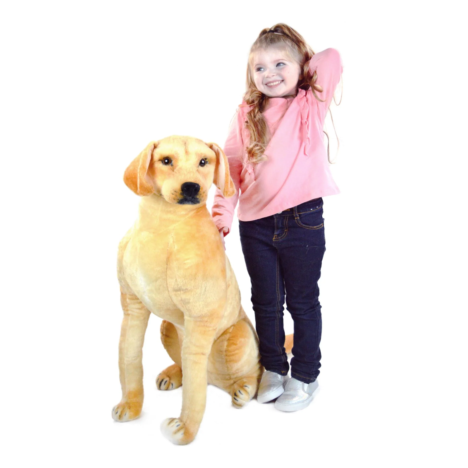 A young girl with blonde pigtails stands next to a very large golden-yellow plush dog on a plain white background.