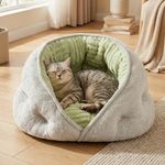 A gray plush cat bed with a green ribbed interior, shown on a wooden floor in a softly lit room with a cat lying inside.