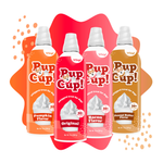 Four Pup Cup! whipped treat cans arranged in a fan shape on a white background with orange and red abstract shapes. The cans are labeled Pumpkin Flavor, Original, Bacon Flavor, and Peanut Butter Flavor.