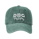 A washed green baseball cap featuring white embroidered text that reads 'DOG mom' with a paw print icon inside the letter O, shown against a plain white background.
