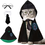 A cat wearing a black wizard-style costume cape with a white collar, black tie, and green crest patch, shown on a white background. The image also includes separate views of the costume pieces: round wire glasses, the white collar, the black tie, and the cape with green lining and crest.