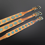 Three tan leather straps laid diagonally on a dark reflective surface, each decorated with repeating turquoise-blue floral tooled studs and finished with silver-toned metal hardware.