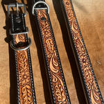 Three brown tooled leather straps with floral embossing and silver metal hardware, laid diagonally on a brown textured surface.