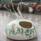 A cream, blue, and green felt pet cave with decorative strings on the top.