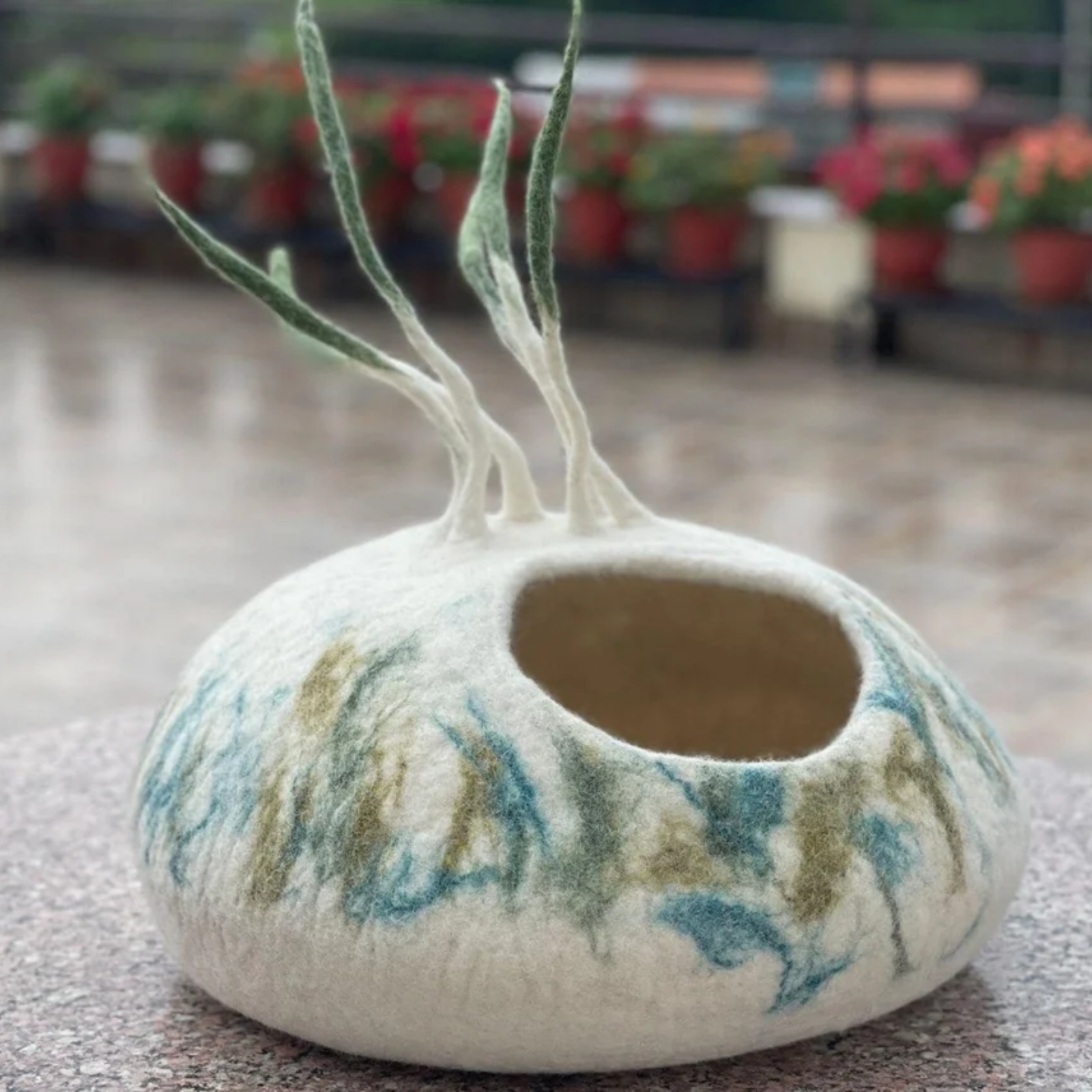 A cream, blue, and green felt pet cave with decorative strings on the top.