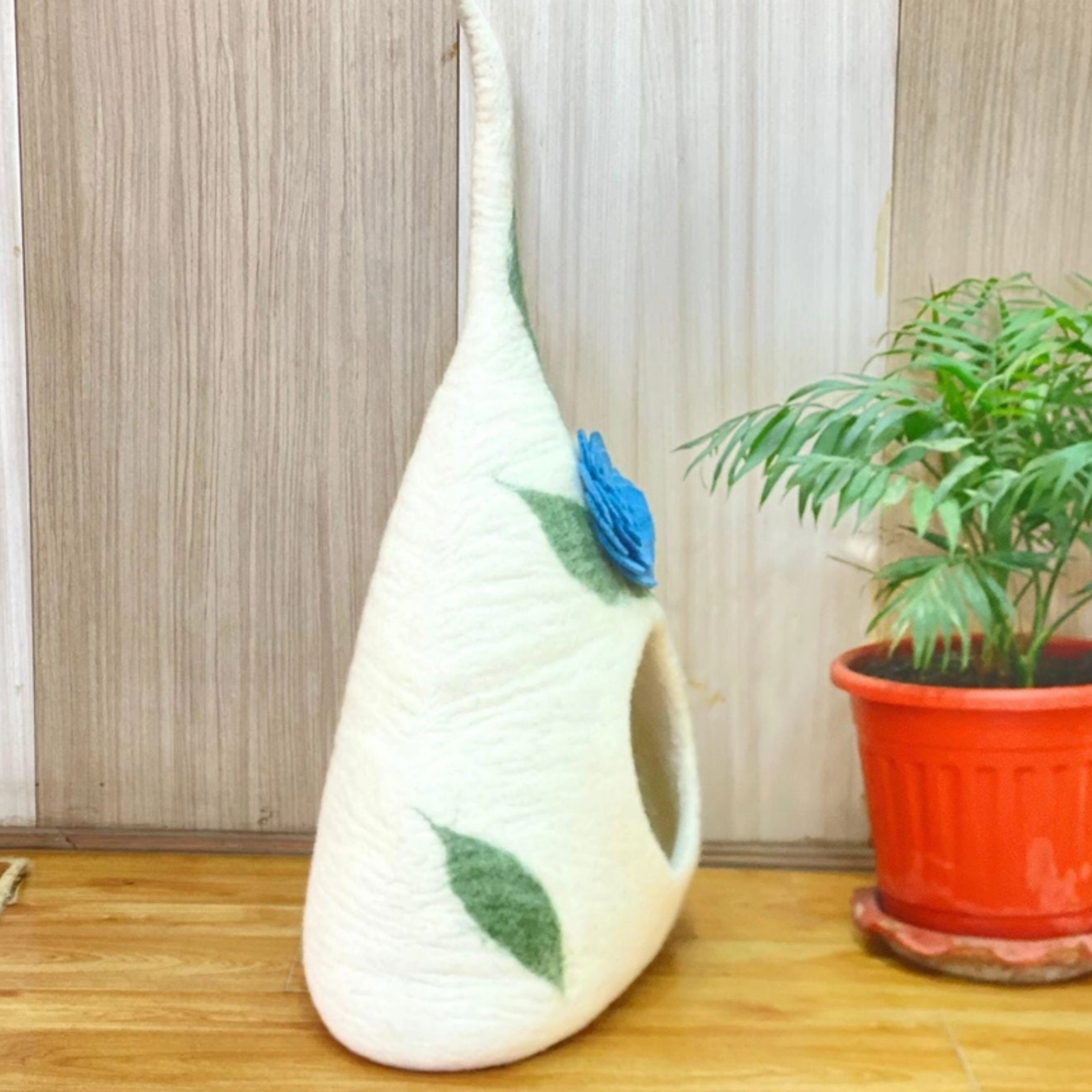 A tall cone-shaped cream felt pet cave with a large blue flower and green vines design shown from the side.