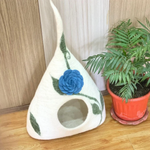 A tall cone-shaped cream felt pet cave with a large blue flower and green vines design.