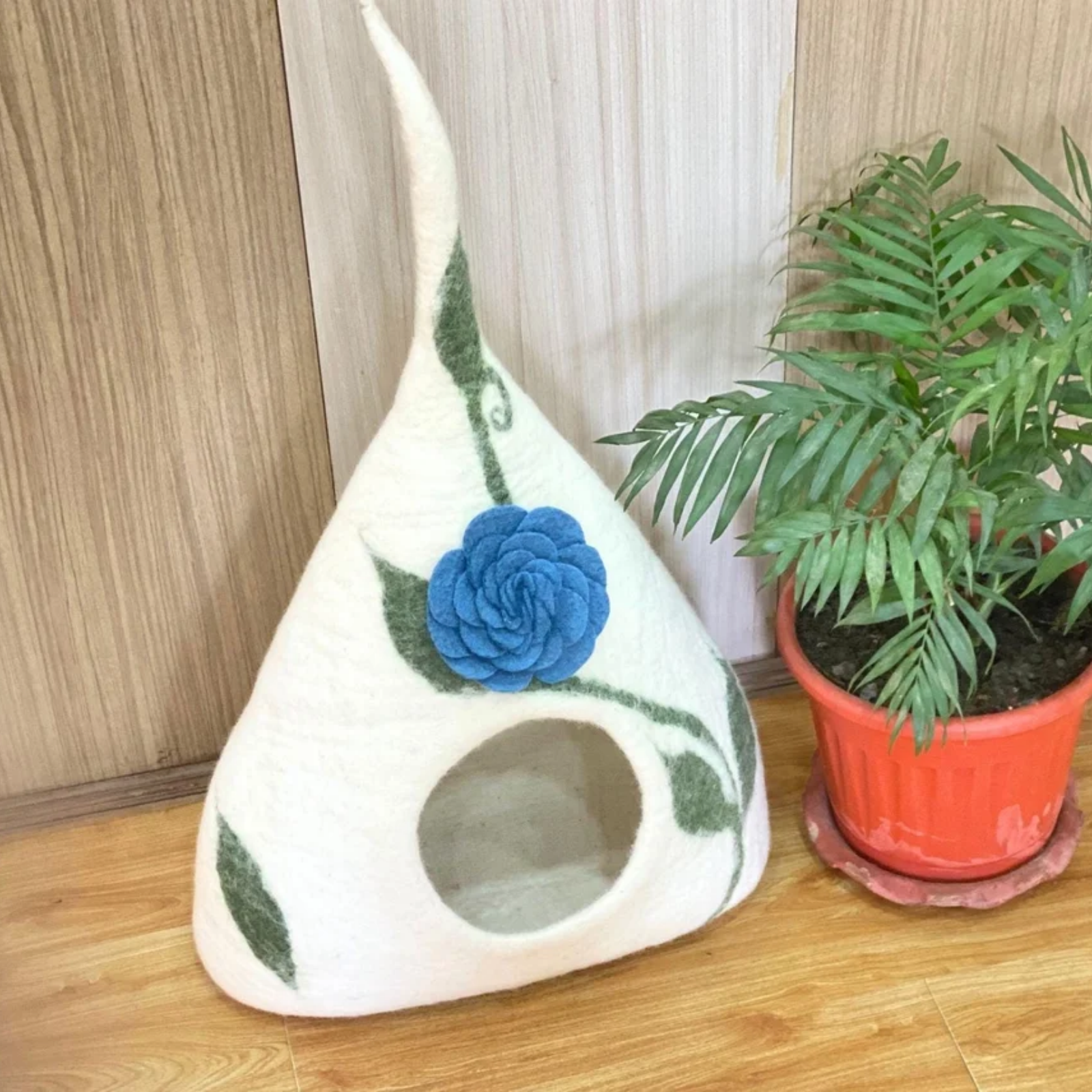 A tall cone-shaped cream felt pet cave with a large blue flower and green vines design.